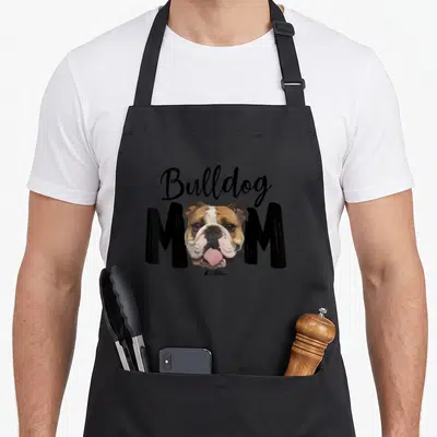 Bulldog bully english aprons - Cartoon Bulldog MOM graphic with dog head replacing O in black text — shown on a black cotton canvas apron against a white background