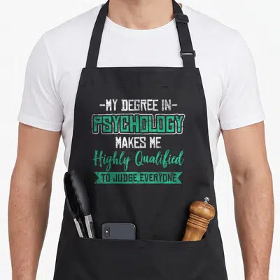 Psychologist science apron - Stacked text psychology degree makes me highly qualified to judge everyone in green ribbon — shown on a black cotton canvas apron against a white background