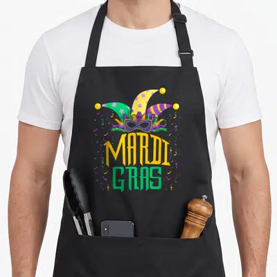 Orlean fat chef apron - Jester hat and mask above MARDI GRAS text in purple, green, yellow with confetti — shown on a black cotton canvas apron against a white background