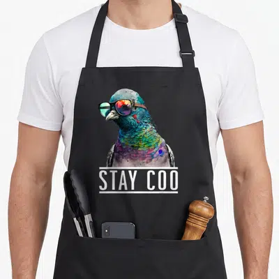 Stay coo bird apron - Multicolored pigeon wearing sunglasses above white banner reading STAY COO — shown on a black cotton canvas apron against a white background
