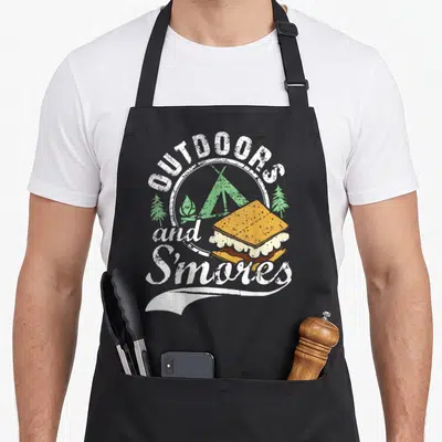 Outdoor camping apron - Distressed Outdoors and S'mores print with green tent and s'more illustration on black apron — shown on a black cotton canvas apron against a white background