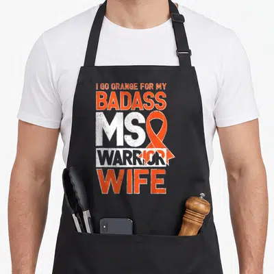 Multiple badass apron - I Go Orange for My Badass MS Warrior Wife with orange ribbon overlay on distressed white — shown on a black cotton canvas apron against a white background
