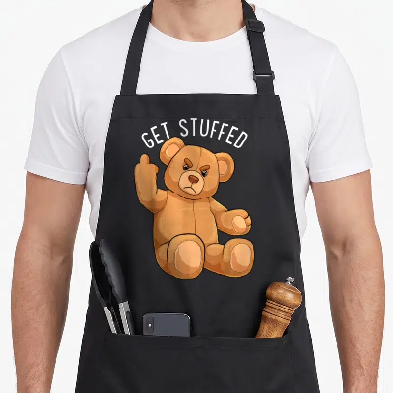 Stuffed teddy bear apron - Brown cartoon bear flipping finger under white arched text GET STUFFED — shown on a black cotton canvas apron against a white background