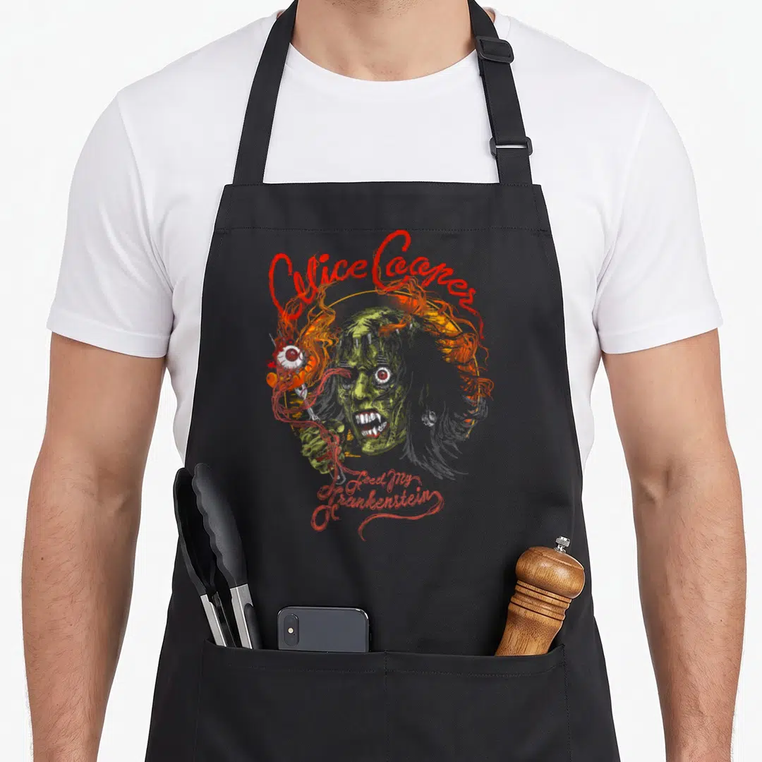 Circle feed apron - Alice Cooper Feed My Frankenstein text over green zombie head in orange circle with distressed red — shown on a black cotton canvas apron against a white background