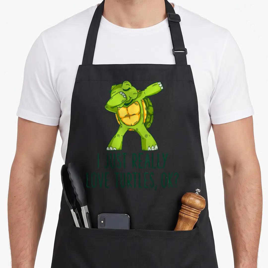 Funny turtle apron - Dabbing green cartoon turtle above text I Just Really Love Turtles Ok — shown on a black cotton canvas apron against a white background