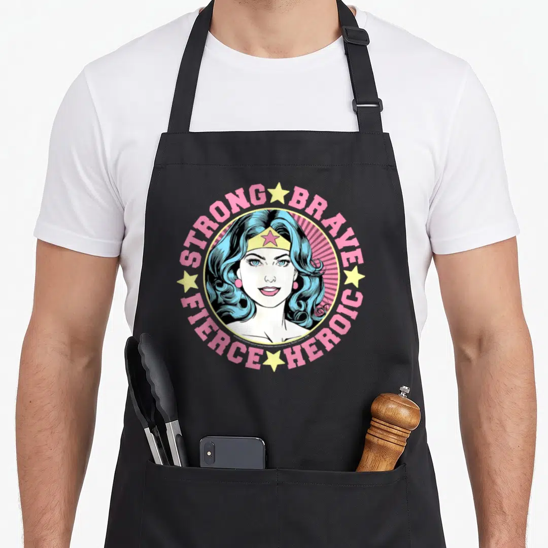 Strong wrap around apron - Vintage Wonder Woman portrait with strong brave heroic fierce text in pink and blue circle — shown on a black cotton canvas apron against a white background