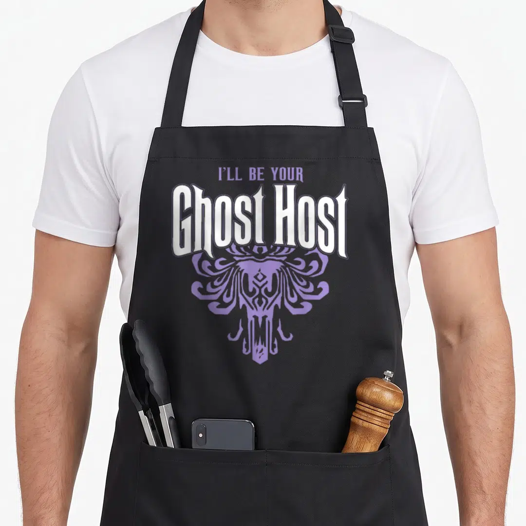 Ill cute halloween aprons - I'll Be Your Ghost Host text above purple stylized ghost figure in cartoon style — shown on a black cotton canvas apron against a white background