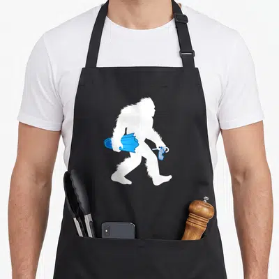 Snorkeling bigfoot apron - White Bigfoot silhouette walking right holding blue cloth and spray bottle — shown on a black cotton canvas apron against a white background