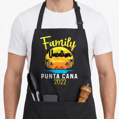 Punta cana family aprons - Family Vacation 2022 sun graphic with palm trees and beach chairs — shown on a black cotton canvas apron against a white background