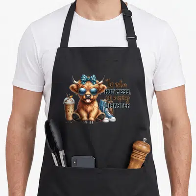 Hot highland cow apron - Cartoon brown highland cow with blue leopard bow, sunglasses, iced drink, shoe, and stacked — shown on a black cotton canvas apron against a white background