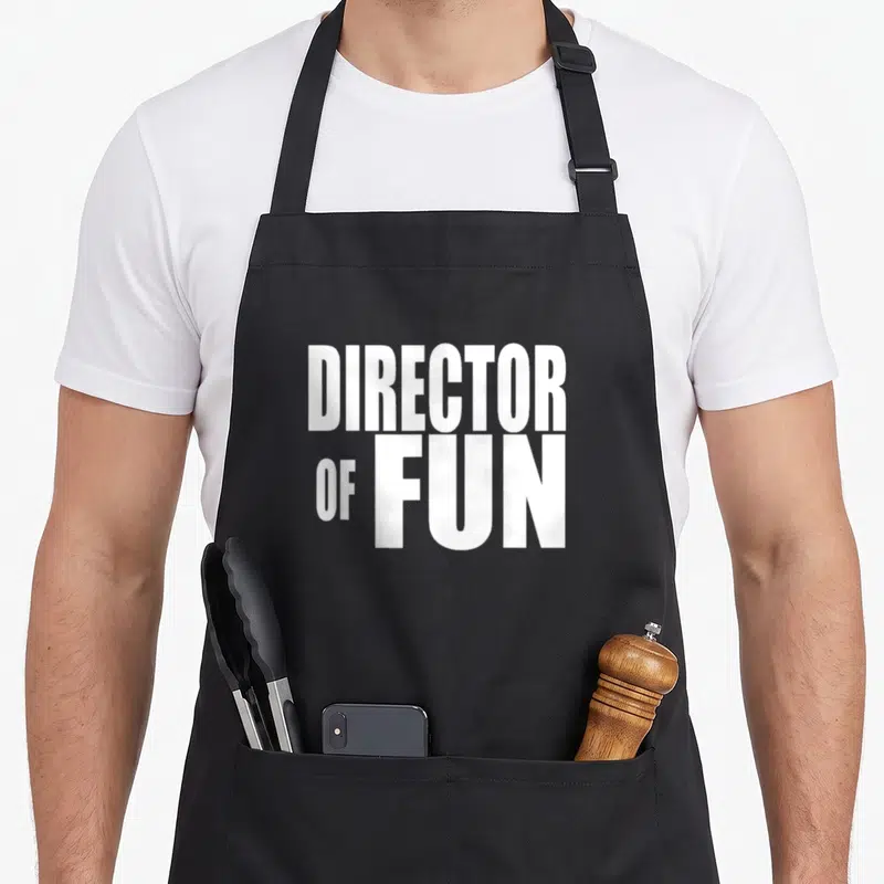 Director wedding planner apron - White stacked text reading DIRECTOR OF FUN on grey background — shown on a black cotton canvas apron against a white background