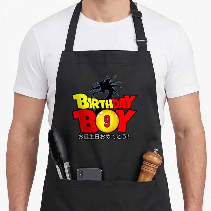 9th anime mom apron - Dragon head over BIRTHDAY BOY text with yellow 9 sphere and Japanese greeting — shown on a black cotton canvas apron against a white background