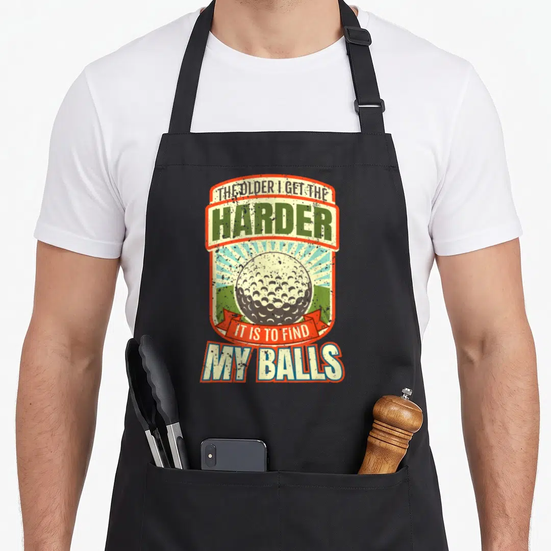 Funny golfer golf apron - Retro golf ball with stacked text THE OLDER I GET THE HARDER IT IS TO FIND MY BALLS and red — shown on a black cotton canvas apron against a white background