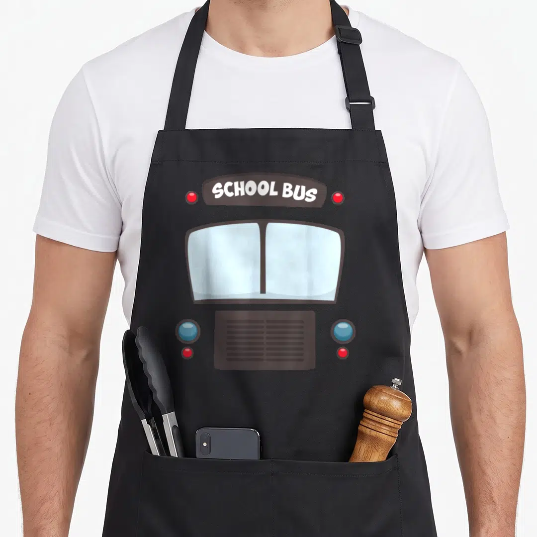 School bus omnibus apron - Cartoon bus front with brown sign reading SCHOOL BUS and blue and red lights — shown on a black cotton canvas apron against a white background