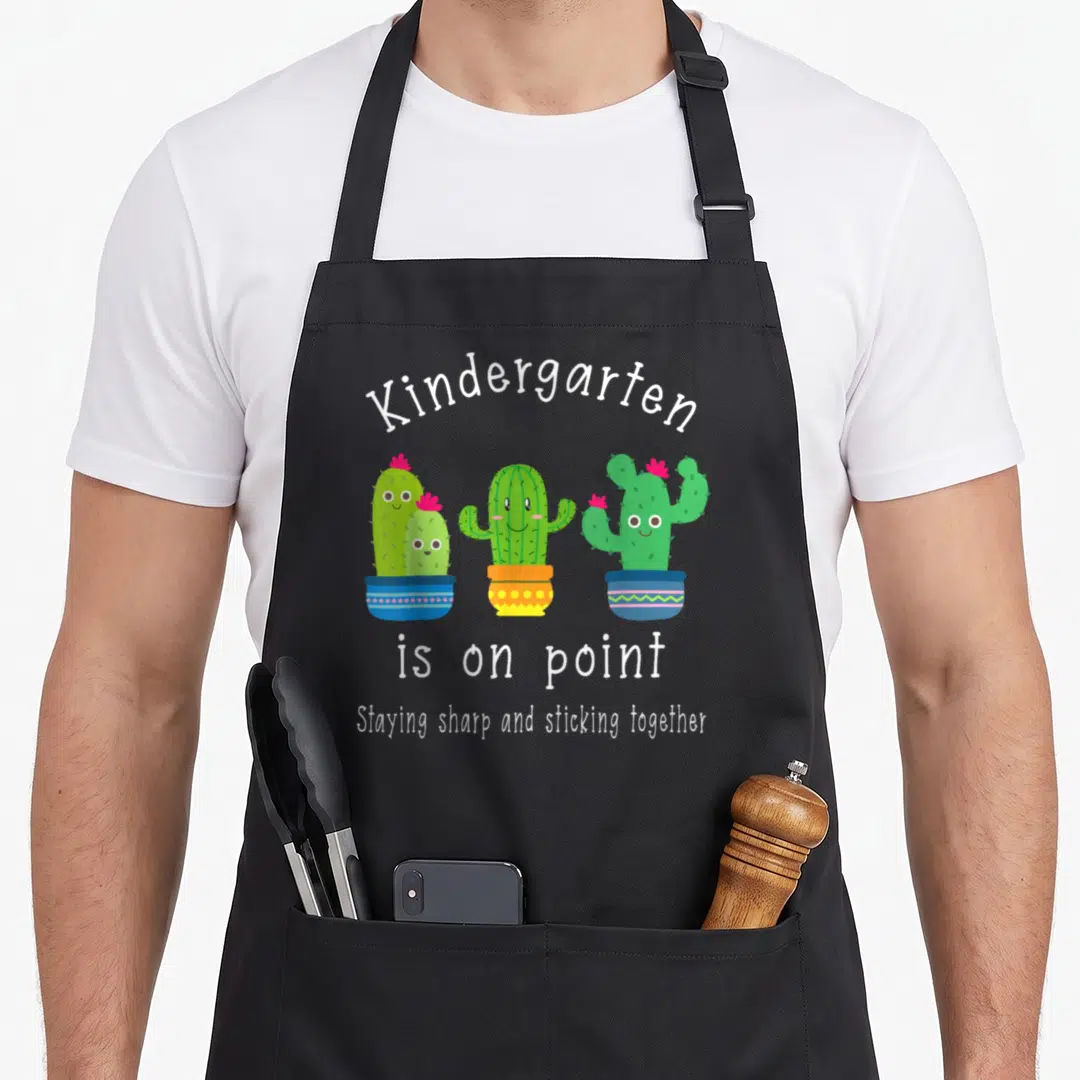Kindergarten classroom aprons - Three cartoon cacti in pots with text Kindergarten is on point — shown on a black cotton canvas apron against a white background