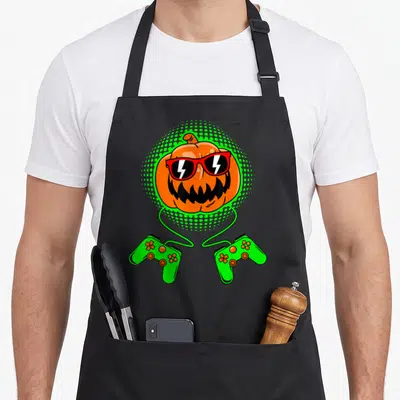 Jack lantern gamer halloween apron - Orange pumpkin wearing red sunglasses in green dotted halo with two green — shown on a black cotton canvas apron against a white background
