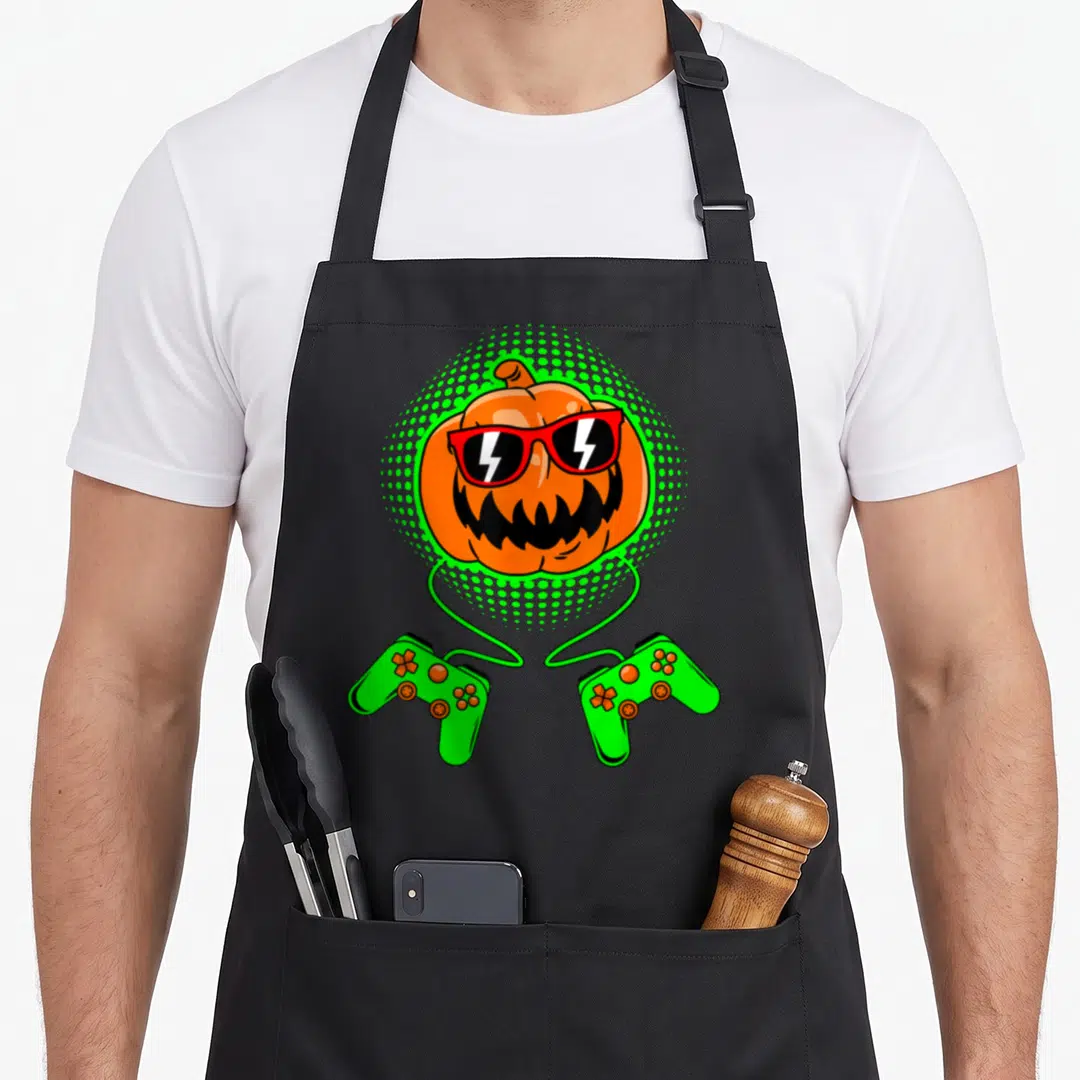 Jack lantern gamer halloween apron - Orange pumpkin wearing red sunglasses in green dotted halo with two green — shown on a black cotton canvas apron against a white background
