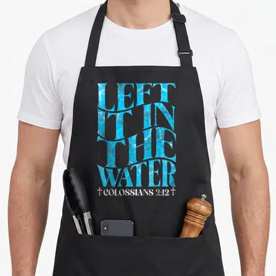 Water christian apron - Blue wavy text Left It In The Water with Colossians 2:12 and two crosses — shown on a black cotton canvas apron against a white background