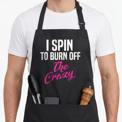 Burn spinning apron - I SPIN TO BURN OFF The Crazy white and pink stacked typography design — shown on a black cotton canvas apron against a white background