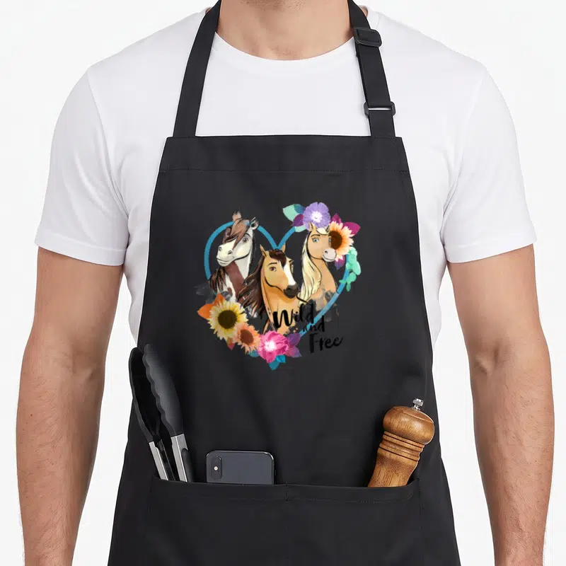 Free novelty apron - Three cartoon horse heads in blue heart with wild and free text and flowers — shown on a black cotton canvas apron against a white background