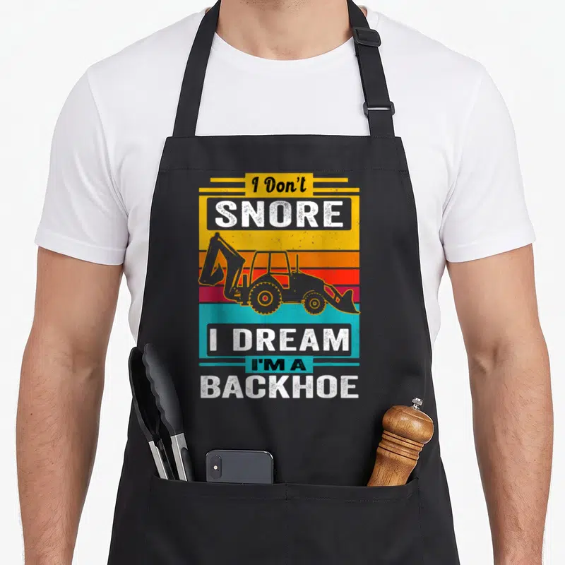 Snore backhoe apron - Retro backhoe graphic on yellow orange red and teal stripes with white distressed text — shown on a black cotton canvas apron against a white background