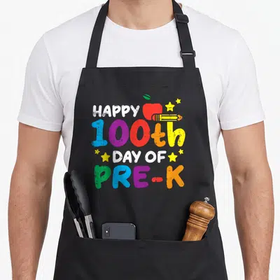 100th pre teacher apron - Stacked colorful text reading Happy 100th Day of Pre-K with red apple yellow pencil — shown on a black cotton canvas apron against a white background