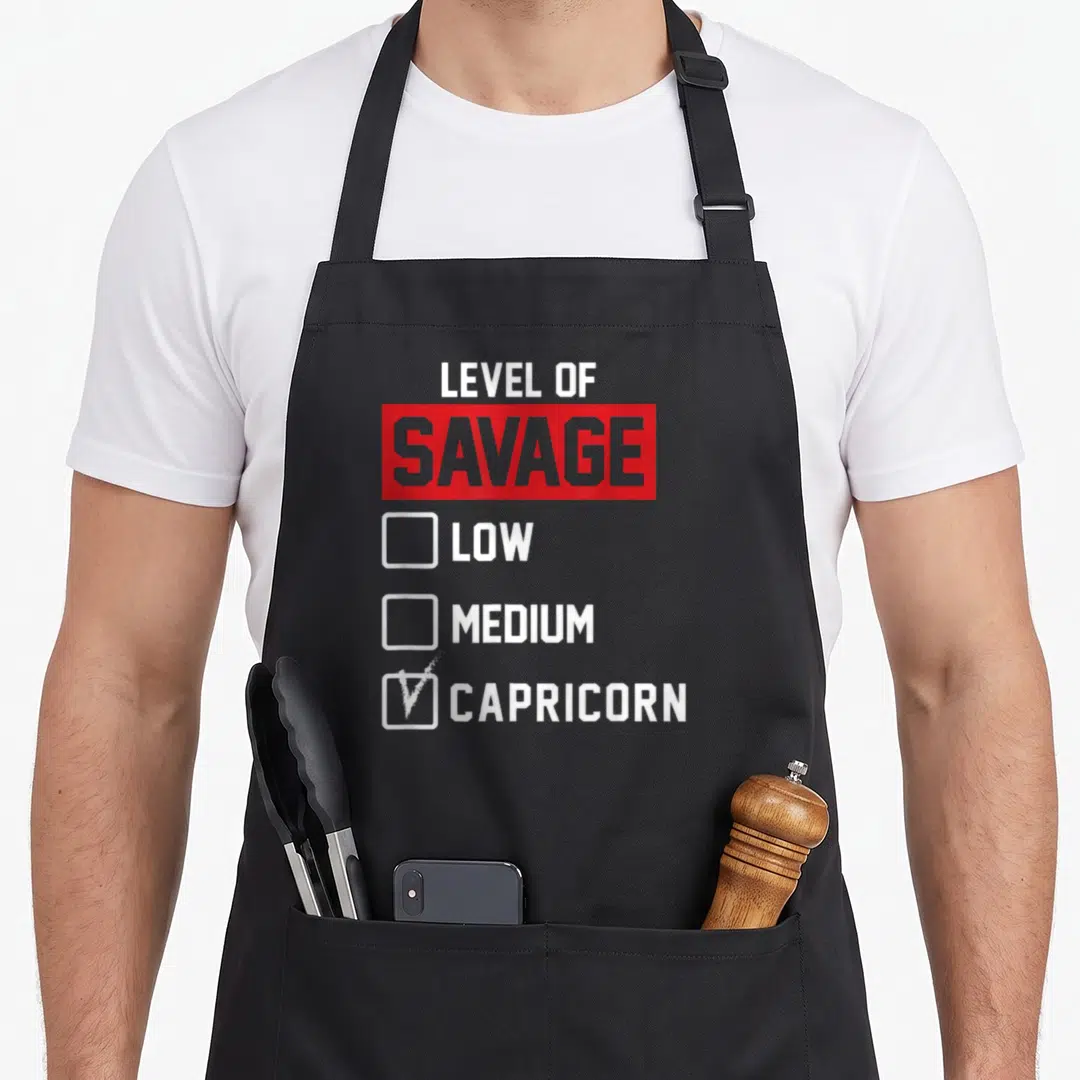 Level savage apron - Checklist graphic with Level of Savage Low Medium Capricorn text and checked box — shown on a black cotton canvas apron against a white background