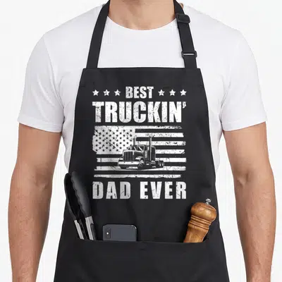 Trucker semi driver apron - White distressed semi-truck over USA flag with Best Truckin' Dad Ever text and stars — shown on a black cotton canvas apron against a white background