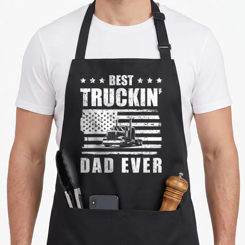 Trucker semi driver apron - White distressed semi-truck over USA flag with Best Truckin' Dad Ever text and stars — shown on a black cotton canvas apron against a white background