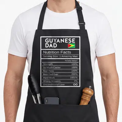 Guyanese nutrition pride apron - Grey nutrition facts label printed with GUYANESE DAD text and small Guyana flag — shown on a black cotton canvas apron against a white background