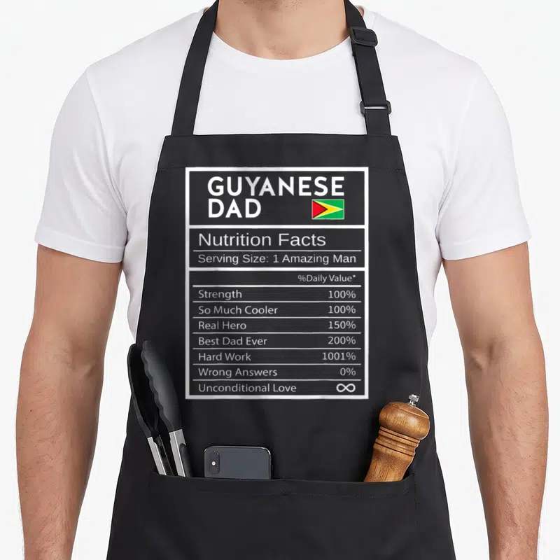 Guyanese nutrition pride apron - Grey nutrition facts label printed with GUYANESE DAD text and small Guyana flag — shown on a black cotton canvas apron against a white background
