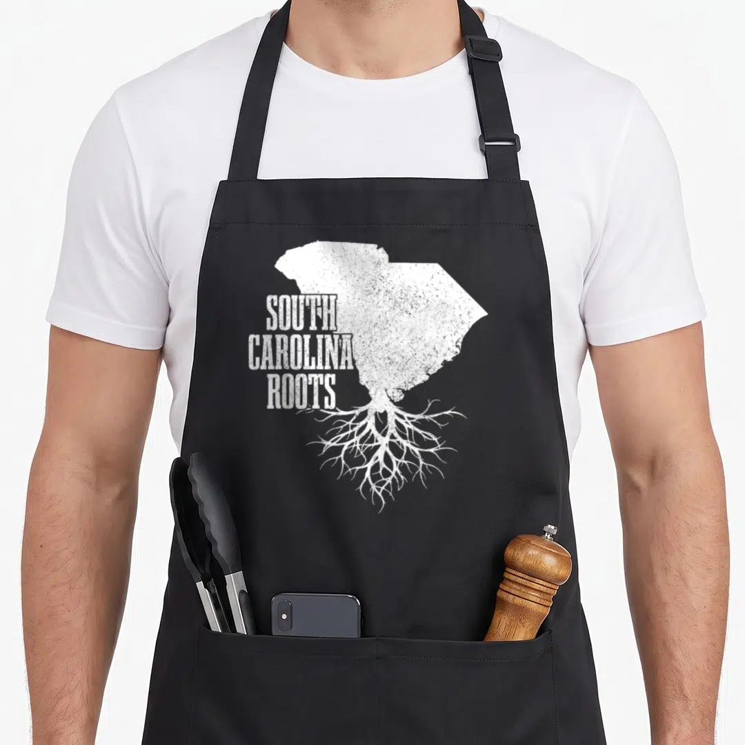 South patriotic apron - White distressed South Carolina map with roots and stacked text reading SOUTH CAROLINA ROOTS — shown on a black cotton canvas apron against a white background