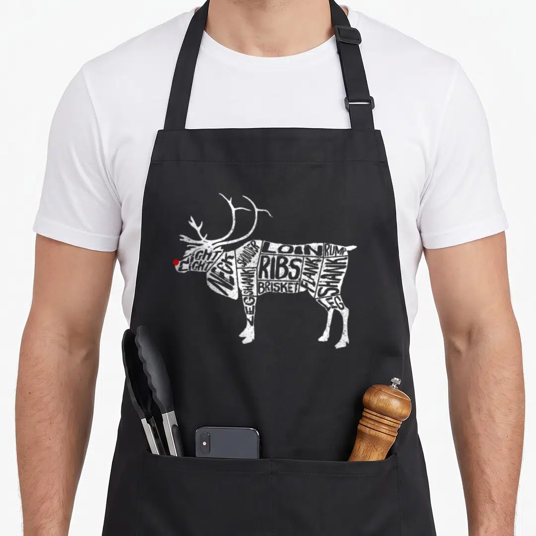 Deer meat cuts apron - Reindeer shape made of meat cut labels like LOIN and RIBS with red nose dot — shown on a black cotton canvas apron against a white background