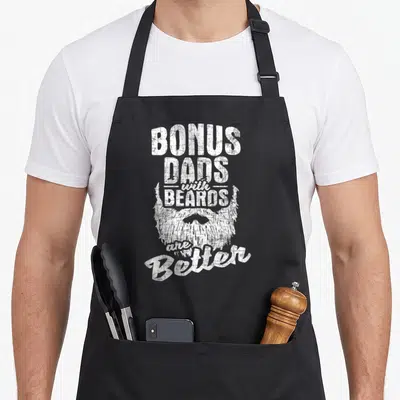 Bonus beard apron - Distressed white text bonus dads with beards better with beard graphic — shown on a black cotton canvas apron against a white background