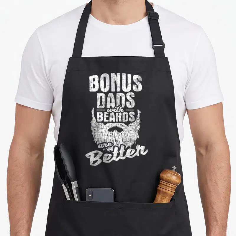 Bonus beard apron - Distressed white text bonus dads with beards better with beard graphic — shown on a black cotton canvas apron against a white background