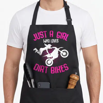 Motocross biking bike apron - White silhouette of girl jumping dirt bike over pink halftone dots with arched text — shown on a black cotton canvas apron against a white background