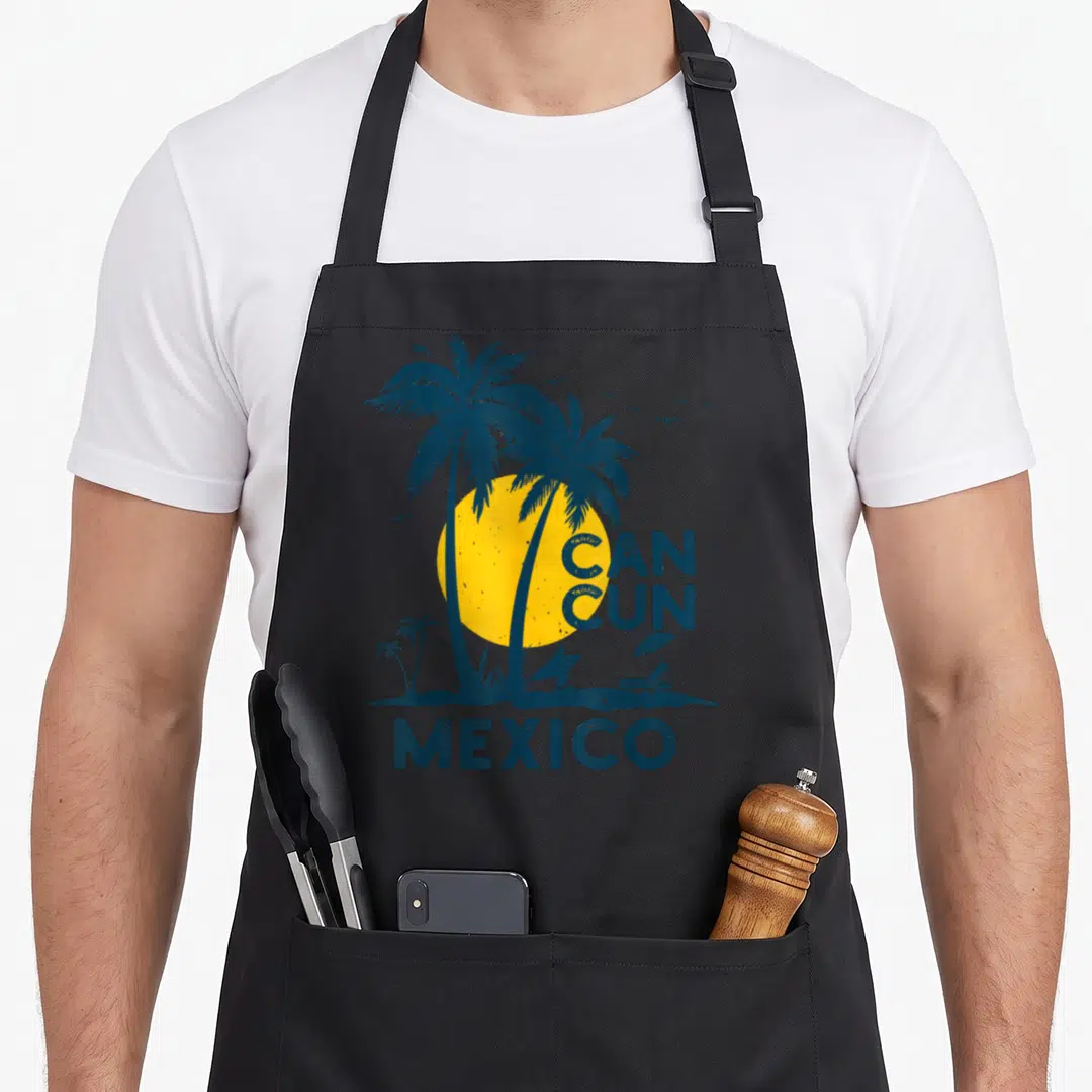 Squad mexico apron - Retro beach scene with yellow sun, two blue palm trees, surfer silhouette, and CAN CUN MEXICO text — shown on a black cotton canvas apron against a white background