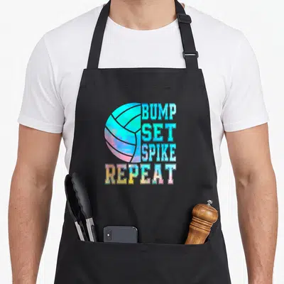 Bump colorful aprons - Watercolor volleyball with stacked text BUMP SET SPIKE REPEAT in blue pink yellow cyan — shown on a black cotton canvas apron against a white background