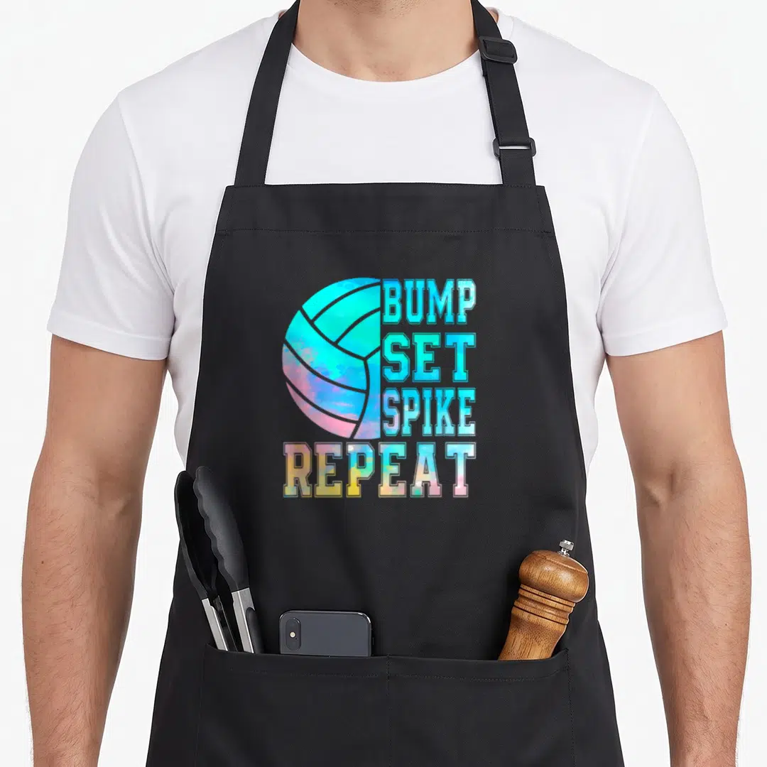 Bump colorful aprons - Watercolor volleyball with stacked text BUMP SET SPIKE REPEAT in blue pink yellow cyan — shown on a black cotton canvas apron against a white background