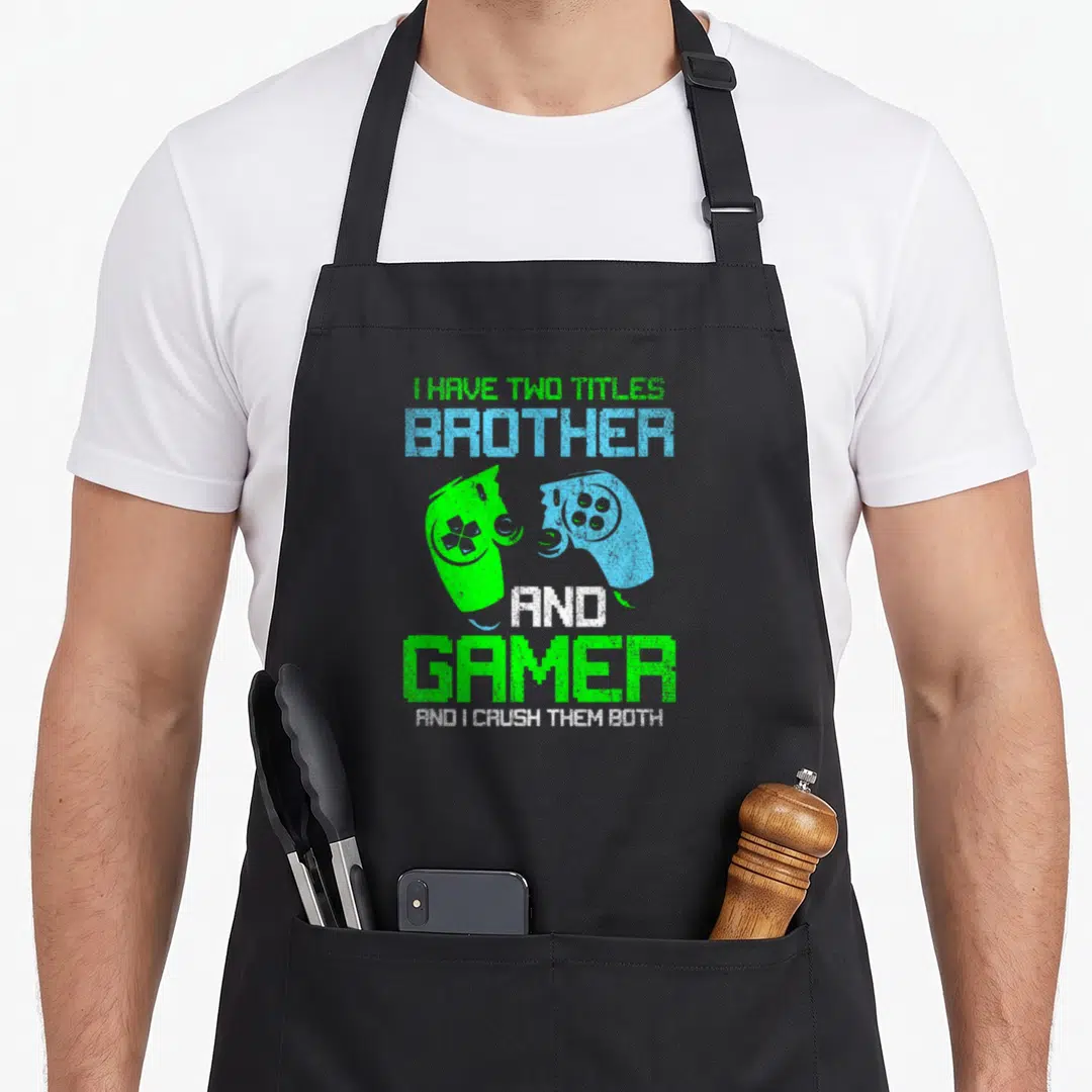 Gamer brother video game apron - Stacked text I HAVE TWO TITLES BROTHER GAMER with two facing green and blue — shown on a black cotton canvas apron against a white background