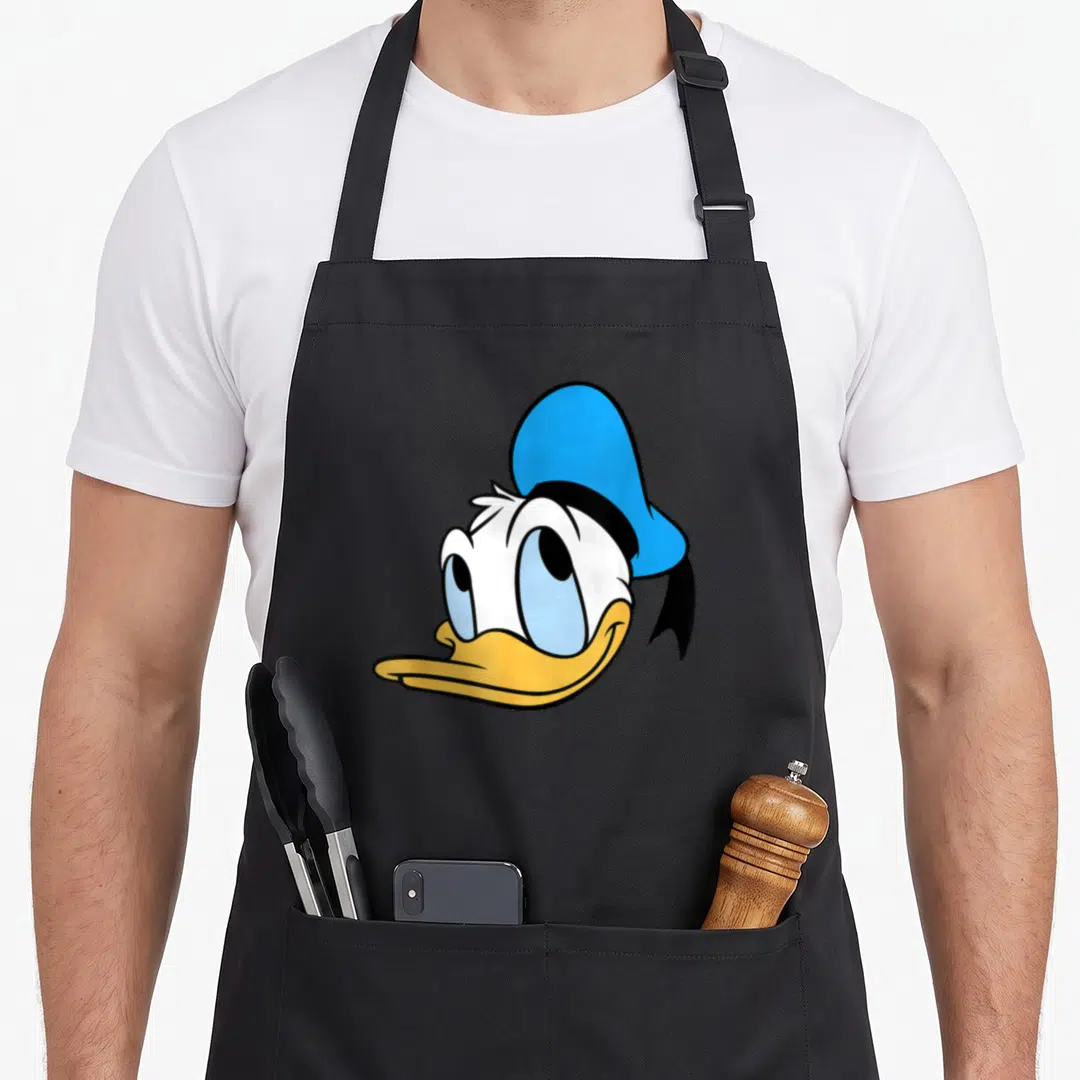 Single crazy duck man apron - Centered cartoon head of Donald Duck with blue hat and yellow beak — shown on a black cotton canvas apron against a white background