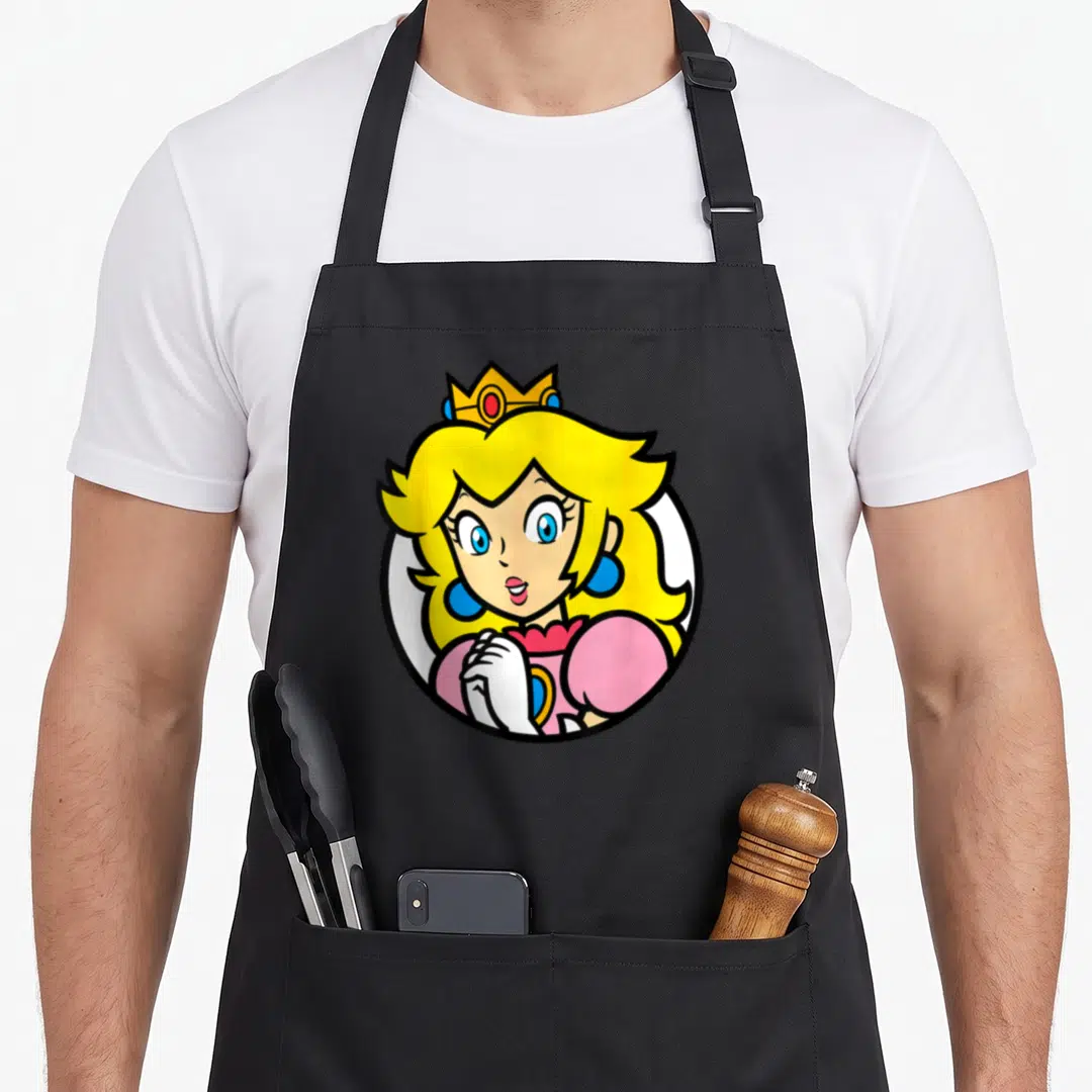 Bro princess apron - Princess Peach cartoon portrait in white circle with yellow hair and pink dress — shown on a black cotton canvas apron against a white background