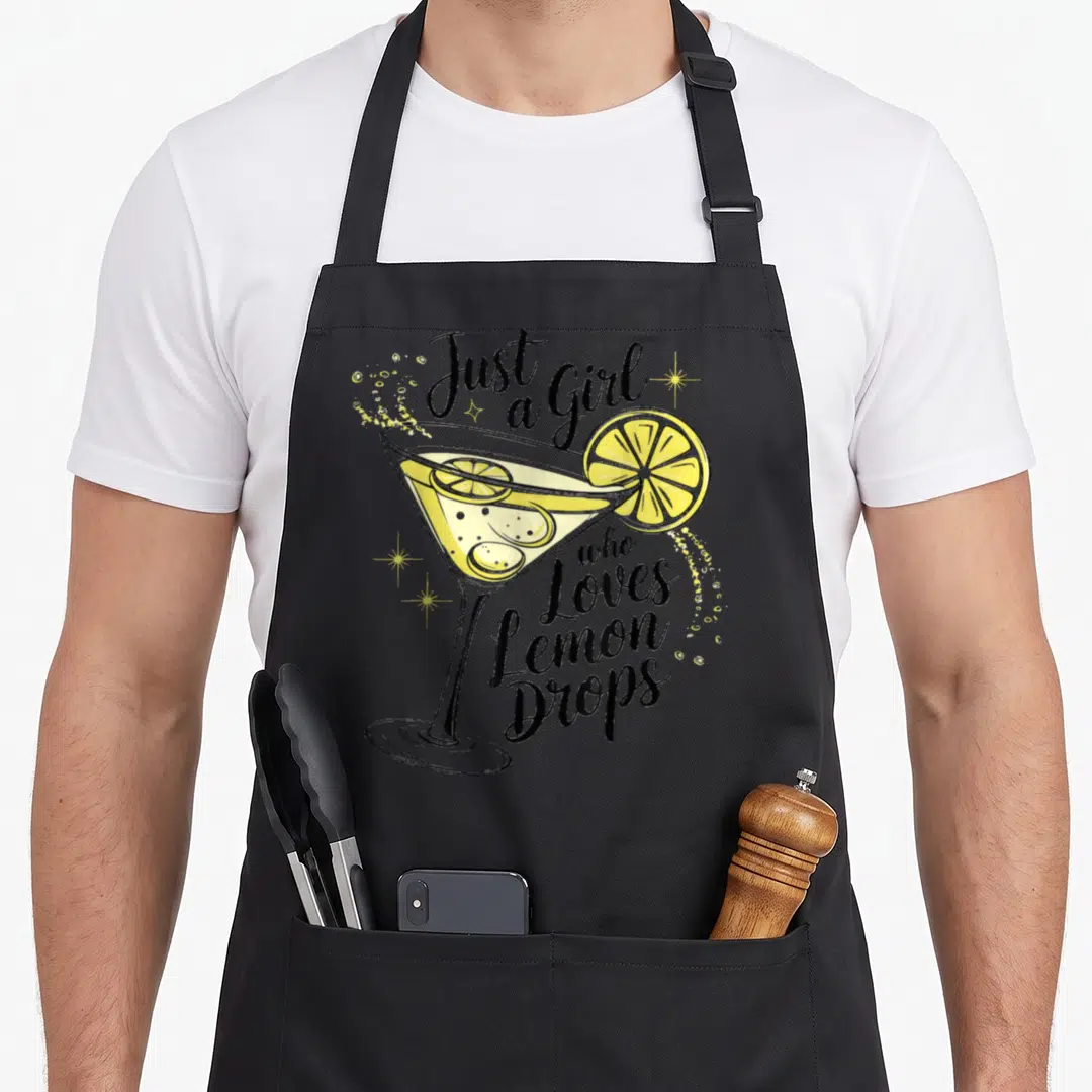 Drinker for love and lemons apron - Cartoon martini glass with lemon slices and black script text reading Just a Girl — shown on a black cotton canvas apron against a white background