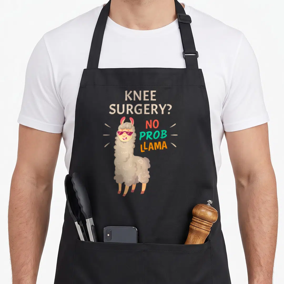 Surgery knee replacement and recovery apron - Cartoon llama in sunglasses with text KNEE SURGERY? NO PROB LLAMA — shown on a black cotton canvas apron against a white background