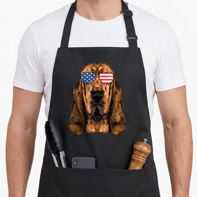 Bloodhound american flag apron - Realistic bloodhound head wearing sunglasses with red white and blue flag pattern — shown on a black cotton canvas apron against a white background
