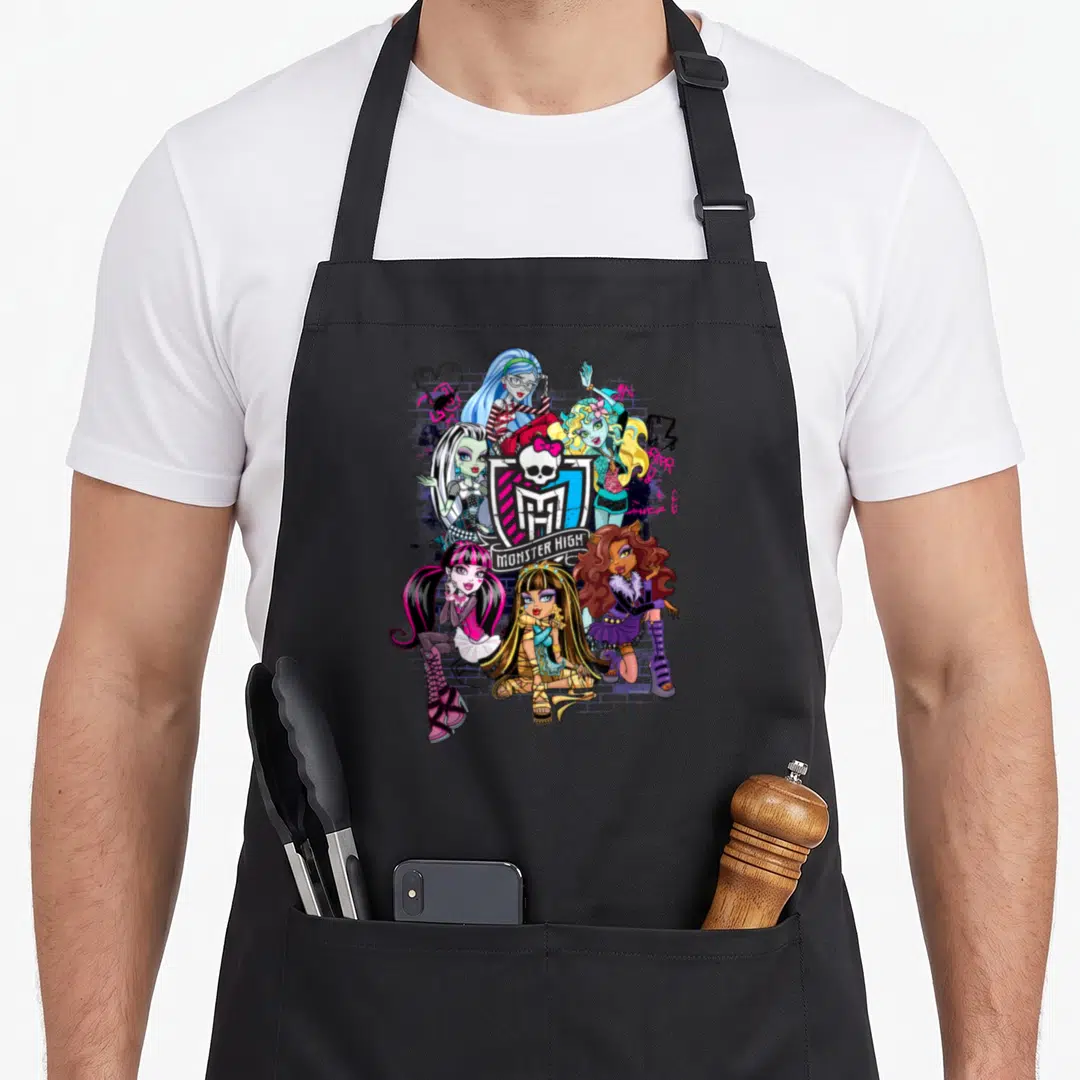 Monster alumni apron - Six cartoon monsters surrounding a skull shield logo with graffiti splatters in pink, blue — shown on a black cotton canvas apron against a white background