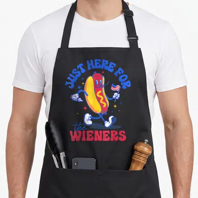 Fourth wiener apron - Cartoon hot dog holding flag and mustard with text JUST HERE FOR the WIENERS — shown on a black cotton canvas apron against a white background