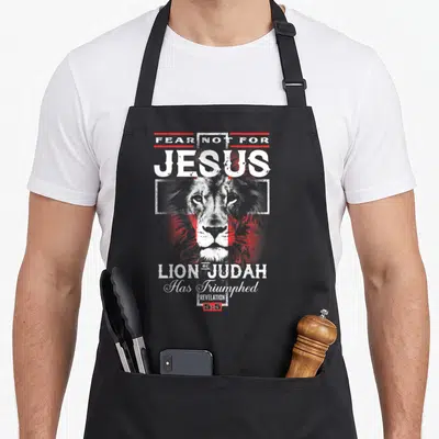 Fear lion apron - Distressed lion head over white cross with red accents and stacked religious text — shown on a black cotton canvas apron against a white background