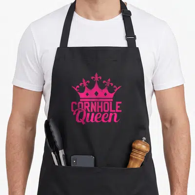 Cornhole queen apron - Pink crown silhouette above stacked text reading CORNHOLE Queen — shown on a black cotton canvas apron against a white background