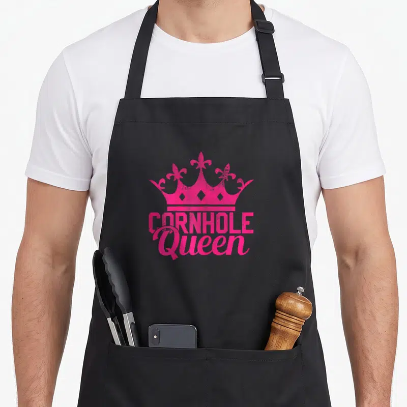 Cornhole queen apron - Pink crown silhouette above stacked text reading CORNHOLE Queen — shown on a black cotton canvas apron against a white background